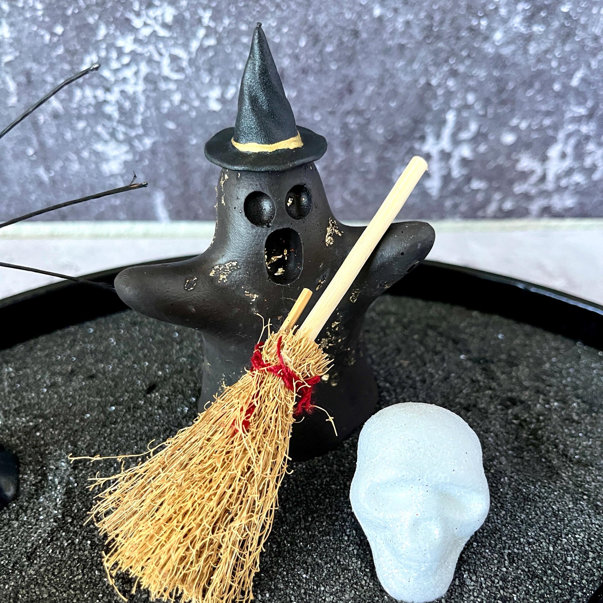 Concrete ghost figurine with witch hat and skull in black sand